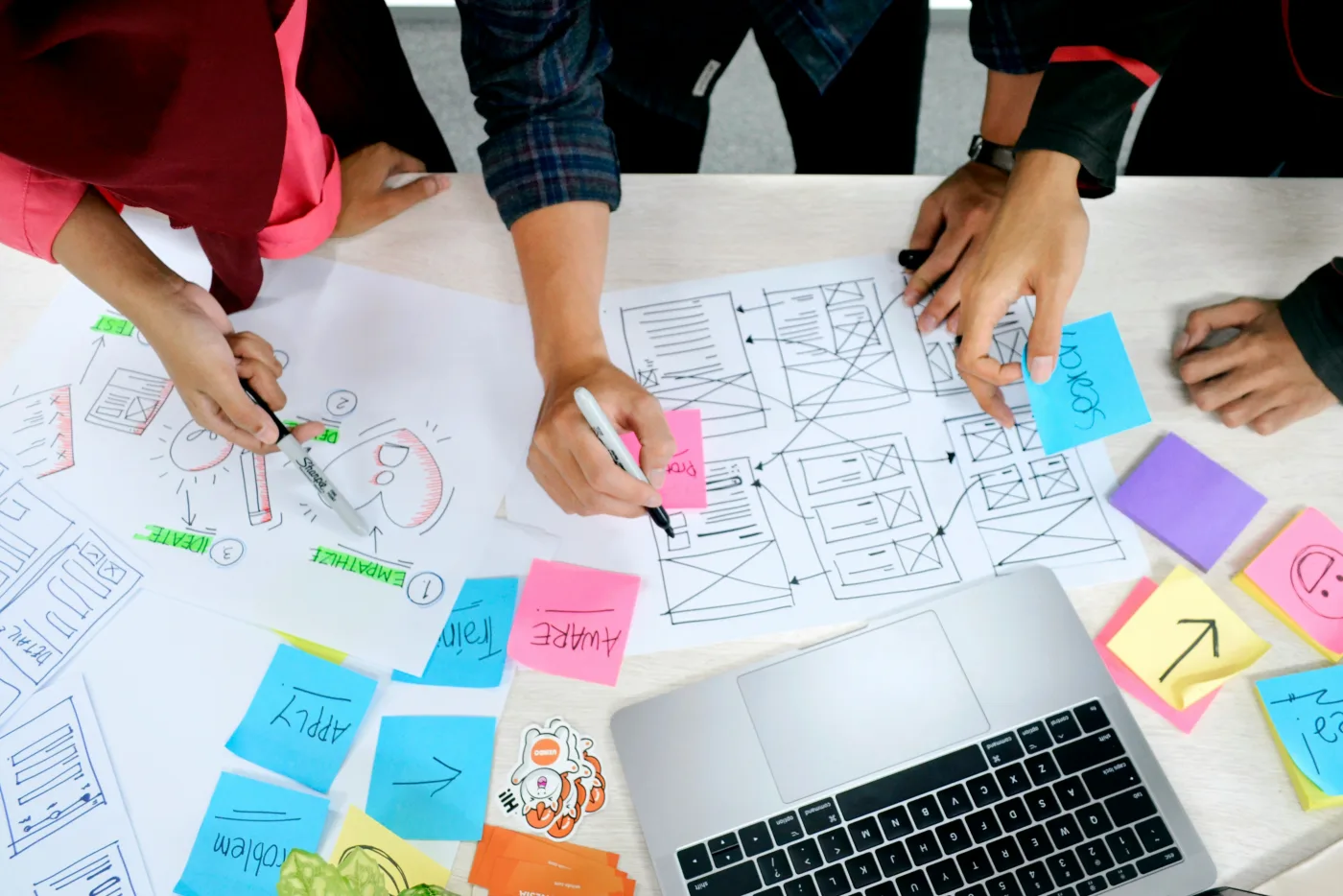 Team sketching ideas and sticky notes around a laptop during a marketing planning workshop